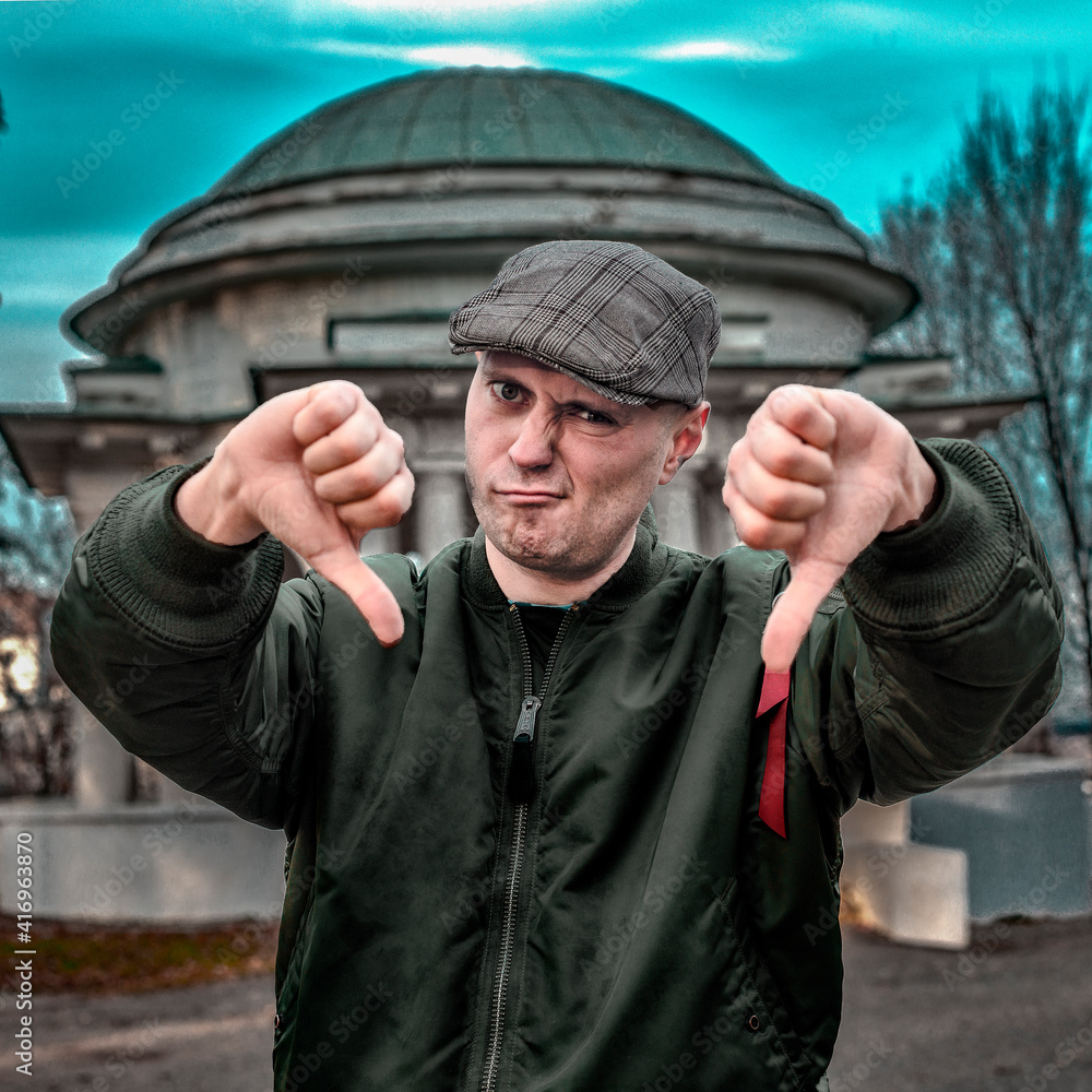 Angry man in a cap shows thumbs down on the city street Angry man in a cap shows thumbs down on the city street