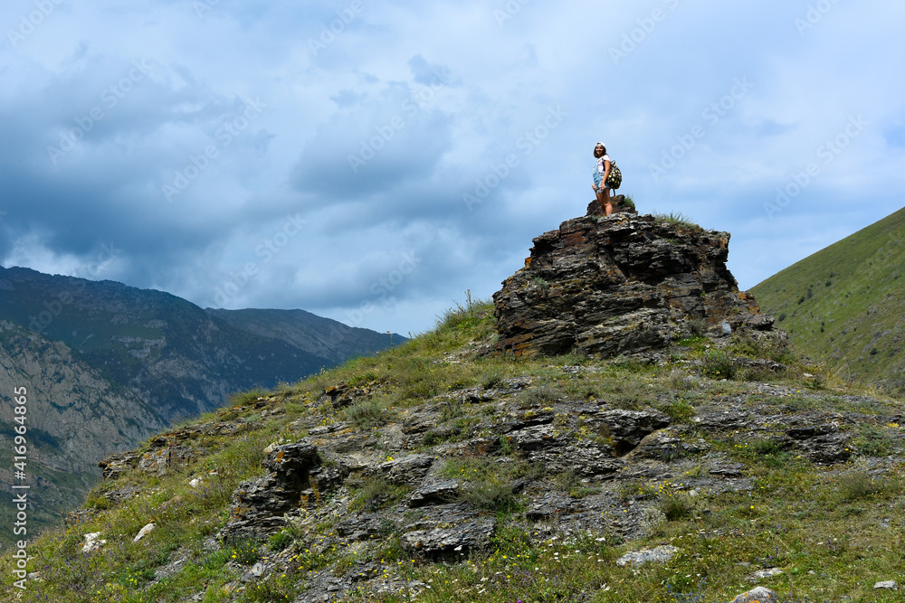 A beautiful young girl stands on a rock in the Kurtat Gorge in the mountains of the North Caucasus. Republic of North Ossetia - Alania