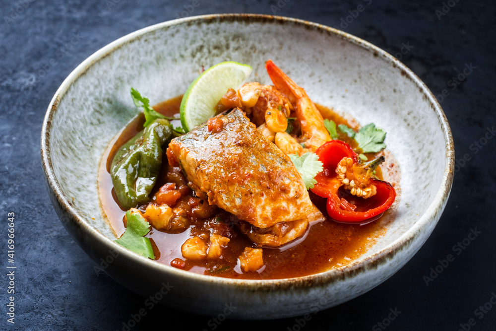 Modern style traditional Mexican seafood pozole soup with fish, king prawns and hominy in a clear sauce served as close-up in design bowl Modern style traditional Mexican seafood pozole soup with fish, king prawns and hominy in a clear sauce served as close-up in design bowl