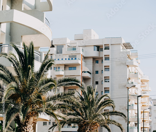 white building with many balconies and windows among palm trees, against the blue sky