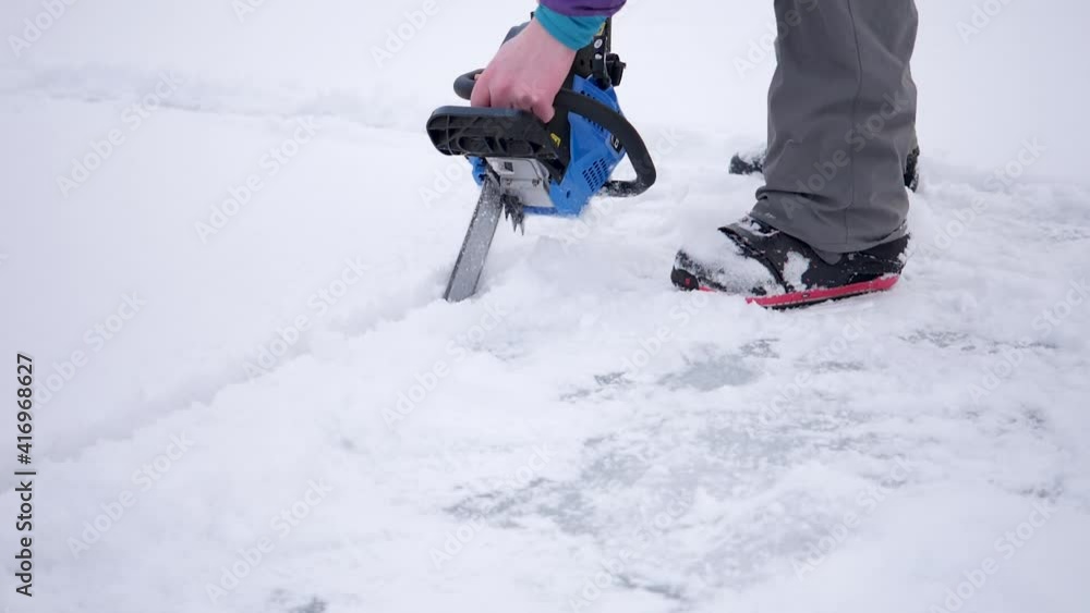 Man with a chainsaw cuts a plunge hole in a frozen lake - slow motion Man with a chainsaw cuts a plunge hole in a frozen lake - slow motion