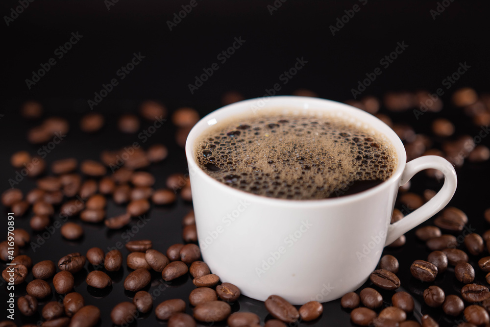 Roasted coffee beans and white mug on black background