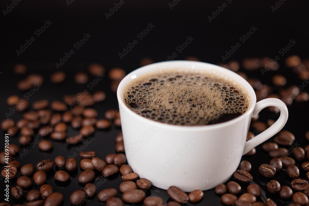 Fototapeta premium Roasted coffee beans and white mug on black background