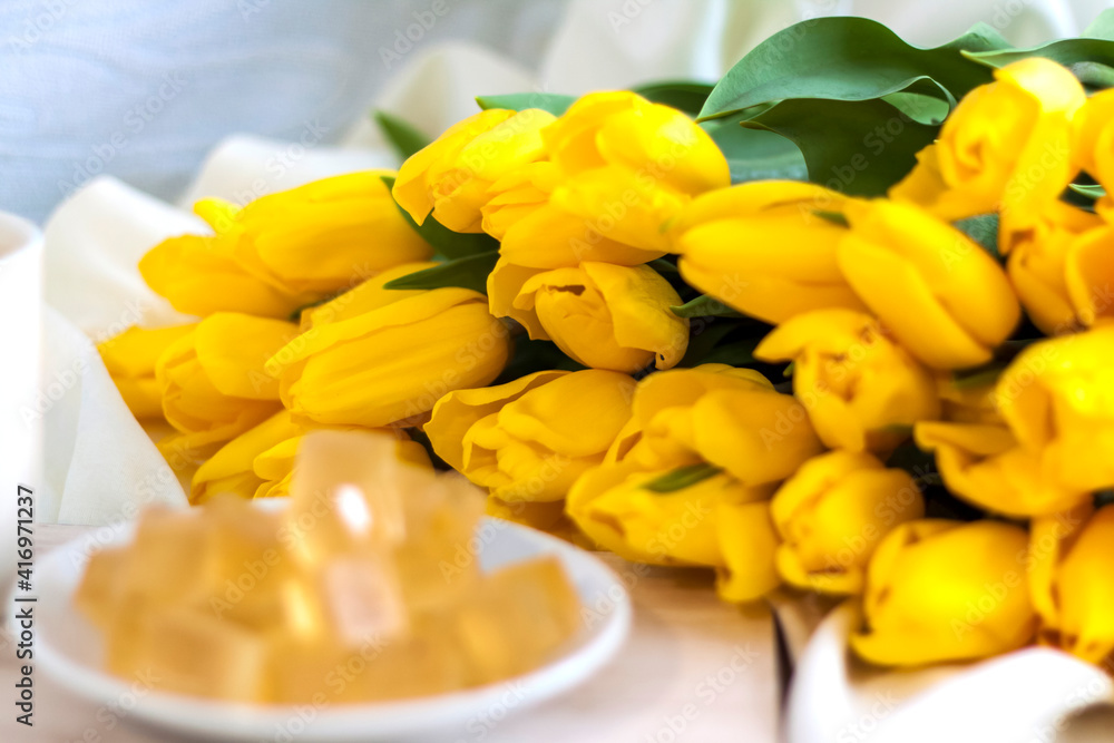 Obraz premium Bouquet of fresh yellow tulips close-up. Flowers in the interior on the background of the bed. Breakfast with coffee and homemade marmalade. The concept of spring and the holiday of March
