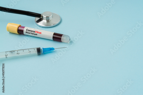 Syringe, stethoscope and blood sample vacuum tube on blue background. Corona virus concept with a copy space.