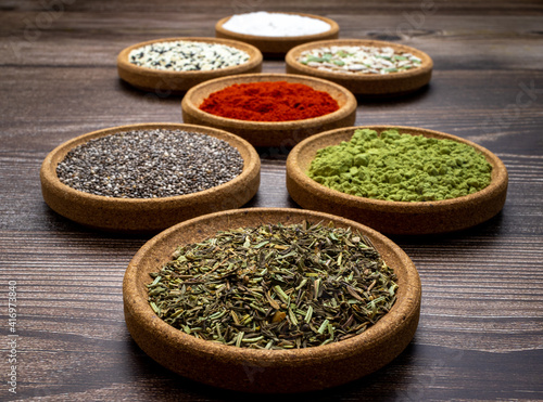Abstract photography of set of cork tree bowls containing colorful spices, french herbs and seeds on wooden surface and backdrop. 