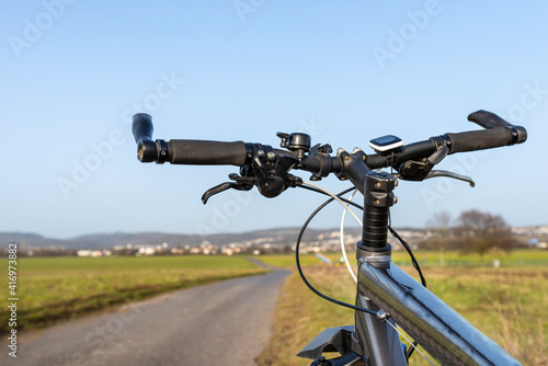 Mountain bike handlebar seen from the first person perspective. Visible bicycle frame and bicycle accessories on the handlebar, and the road in the background. © Michal