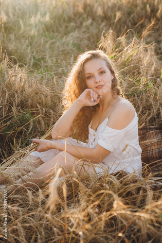 Girl with long curly hair poses in a wheat field