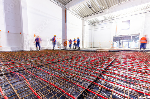 Fotografija Workers do concrete screed on floor with heating in a new warehouse building