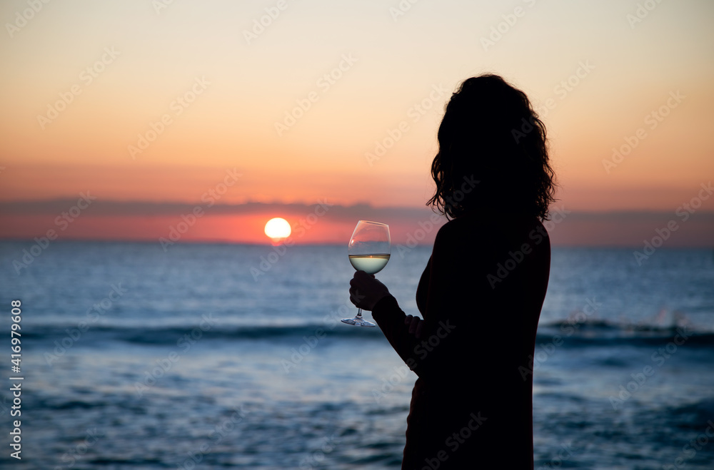 girl has a glass of wine in front of the sea at sunset