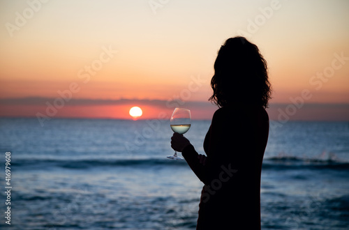 girl has a glass of wine in front of the sea at sunset