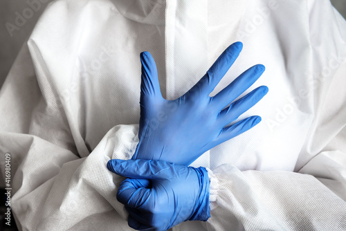 Doctor or nurse in white medical PPE suit puts on protective gloves photo