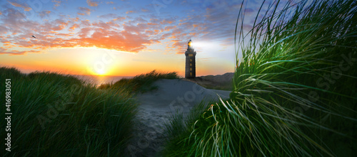 Lighthouse with beacon on coast in windy stormy sea and beach with dunes and grass