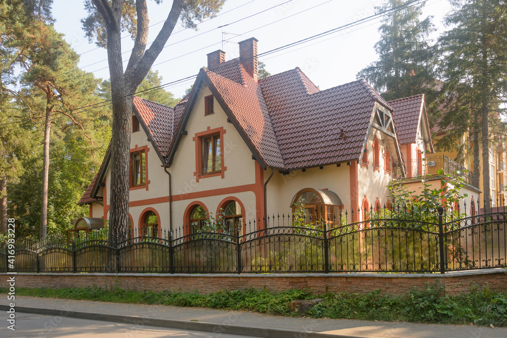 Modern private house with attic floor. Wrought iron fence and large conifers Modern private house with attic floor. Wrought iron fence and large conifers