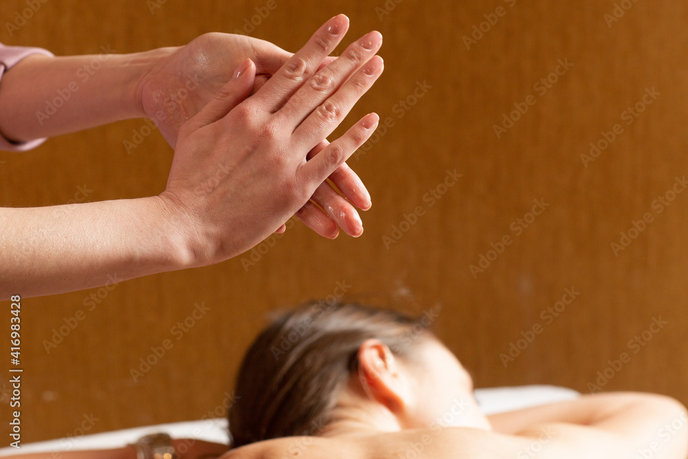 Masseuse preparing for doing aromatherapy oil massage in spa salon. Close-up of the hands of a masseuse rubbing the aroma oil. Young woman relaxing on a couch. Body care, massage, spa concept. Masseuse preparing for doing aromatherapy oil massage in spa salon. Close-up of the hands of a masseuse rubbing the aroma oil. Young woman relaxing on a couch. Body care, massage, spa concept.