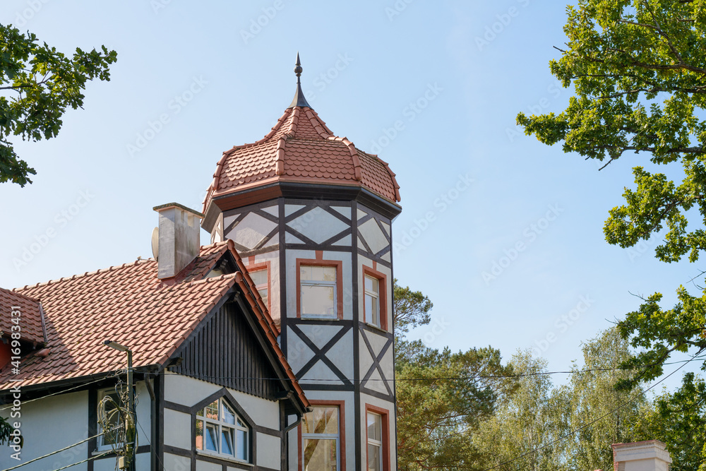 Building is tower with windows and half-timbered decoration. Roof made of red tiles in form dome with spire. German architecture. Close-up, selective focus Building is tower with windows and half-timbered decoration. Roof made of red tiles in form dome with spire. German architecture. Close-up, selective focus