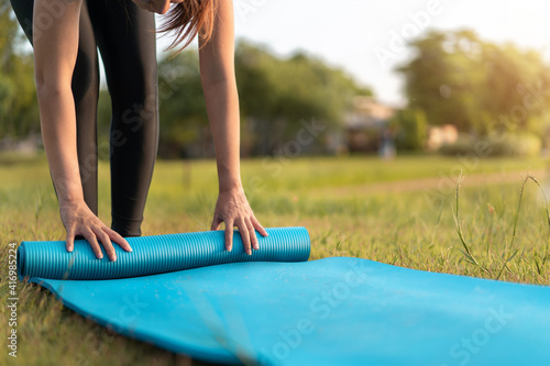 Fototapeta Naklejka Na Ścianę i Meble -  Young asian woman rolling blue yoga mat or fitness mat prepare to exercise in park, Healthy concept, Mind-body improvements concept.
