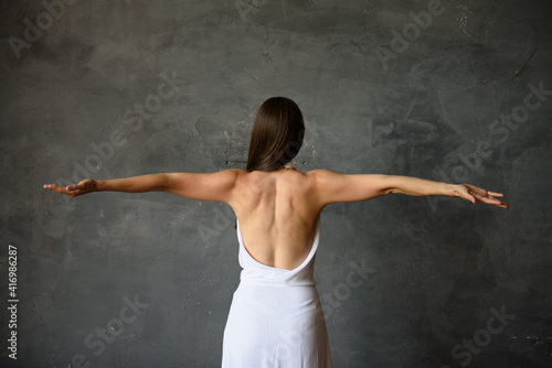 athletic healthy back of a girl in a white dress. gray wall