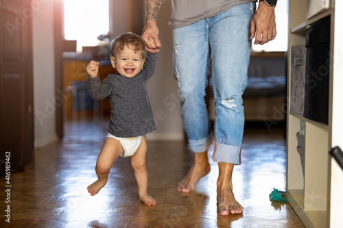 Quadro em tela Little boy learning to walk with his father next to him at home