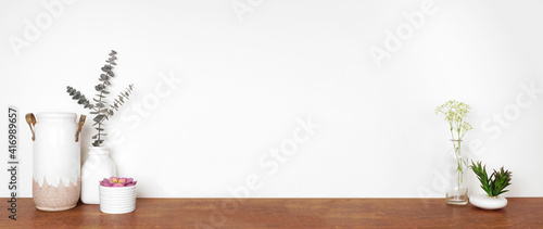 Home decor on a shelf. Vases, succulent plants and branches. Wood shelf against a white wall. Banner with copy space.