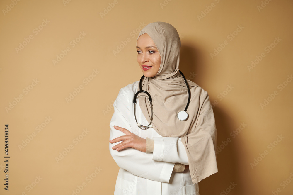 Beautiful serene Muslim doctor woman in hijab standing with crossed