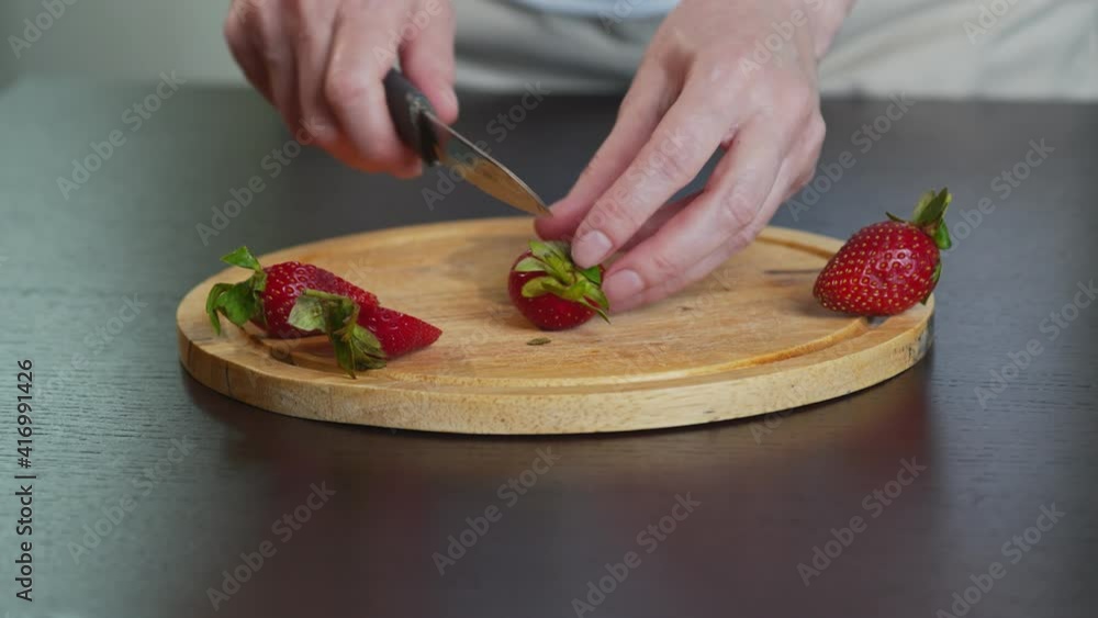 Close-up of a young girl cutting fresh ripe strawberries with a knife on a wooden cutting Board on a metal table. Close-up of a young girl cutting fresh ripe strawberries with a knife on a wooden cutting Board on a metal table.