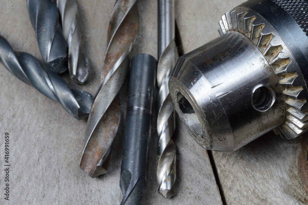 replaceable drill chuck and old drill bits lie on a wooden plank background. close-up. replaceable drill chuck and old drill bits lie on a wooden plank background. close-up.