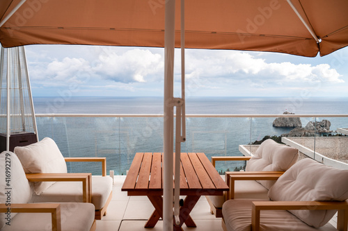 Restaurant with sea view. You can see rocks in the sea. Wooden tables and chairs with white cushions. Overcast, cloudy weather. © svetograph