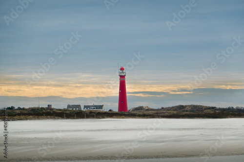 View on the red lighthouse of the Dutch island Schiermonnikoog over a beach  storm blowing sand over the beach