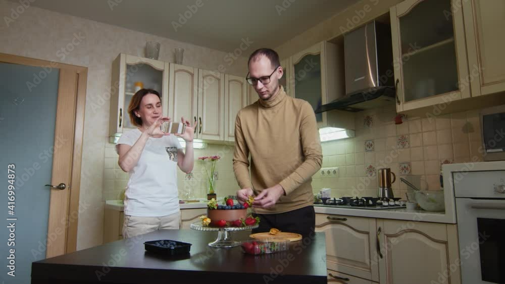 Male chef man decorates the chocolate cake with berries, and his wife makes a video of it Male chef man decorates the chocolate cake with berries, and his wife makes a video of it