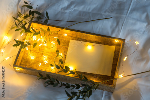 A eucalyptus branch lies on a white sheet beside a tray with a cup of tea and a saucer in a letter in an envelope. The garland is glowing.