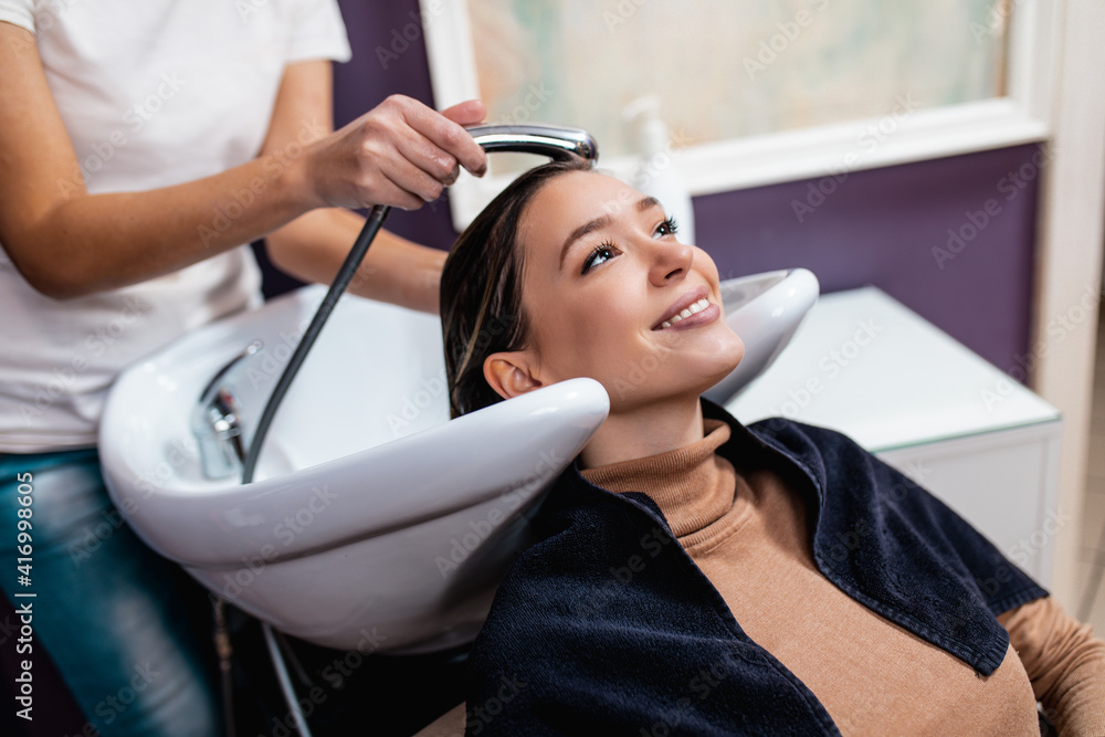 Professional hairdresser washing hair of a beautiful young adult woman in hair salon. Professional hairdresser washing hair of a beautiful young adult woman in hair salon.