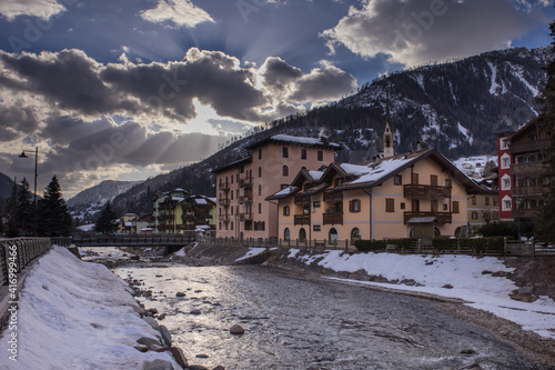 Houses and hotels in Moena, a city in italian Val di Fassa on a sunny winter day rising over the river in the centre