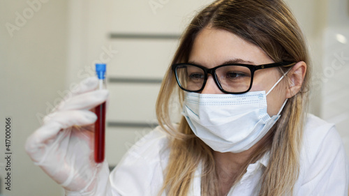 Female scientist holding test tube with blood sample. The concept of analyzes and diagnostics of viruses and diseases.