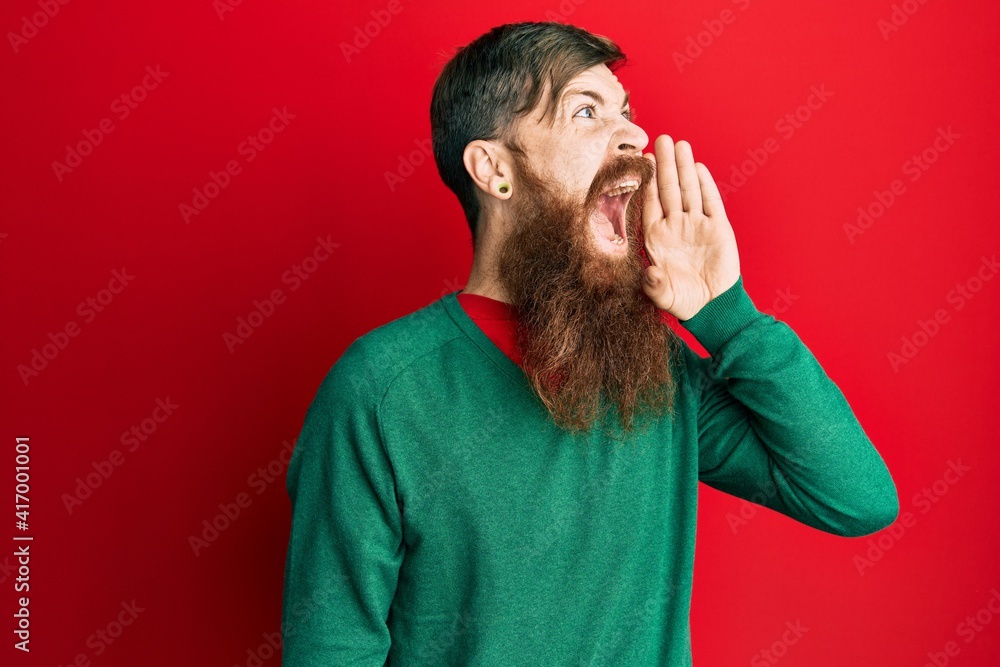 Redhead man with long beard wearing casual clothes shouting and screaming loud to side with hand on mouth. communication concept. Redhead man with long beard wearing casual clothes shouting and screaming loud to side with hand on mouth. communication concept.