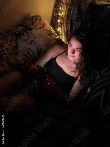 young womans face iluminated with her phone on the couch