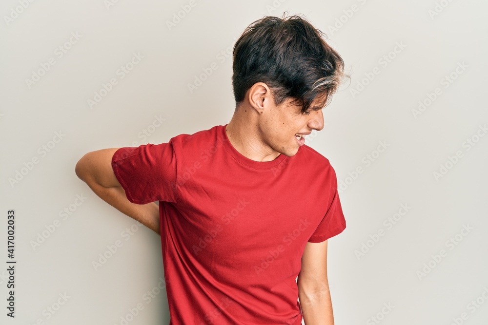 Young hispanic man wearing casual clothes suffering of backache, touching back with hand, muscular pain Young hispanic man wearing casual clothes suffering of backache, touching back with hand, muscular pain