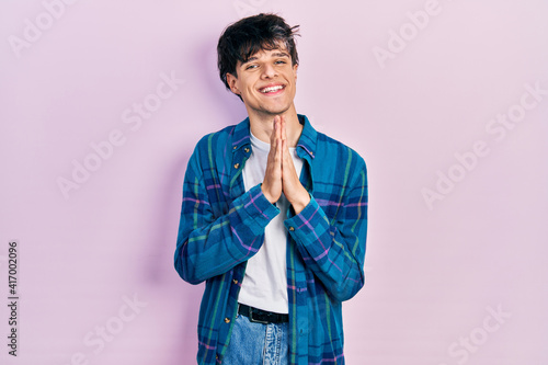 Handsome hipster young man wearing casual white t shirt and vintage shirt praying with hands together asking for forgiveness smiling confident.