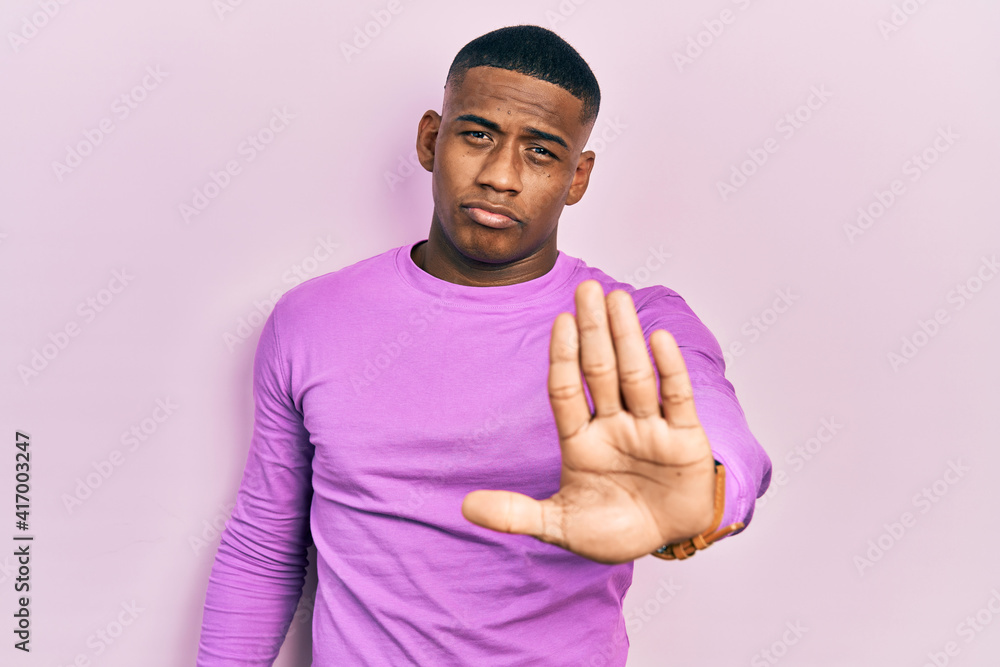 Young black man wearing casual pink sweater doing stop sing with palm of the hand. warning expression with negative and serious gesture on the face. Young black man wearing casual pink sweater doing stop sing with palm of the hand. warning expression with negative and serious gesture on the face.