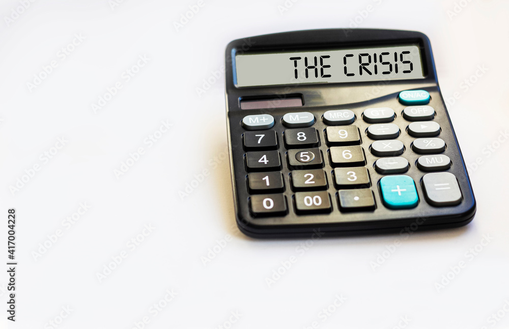 Calculator with the inscription THE CRISIS lies on a white background in the office. Business concept. Calculator with the inscription THE CRISIS lies on a white background in the office. Business concept.