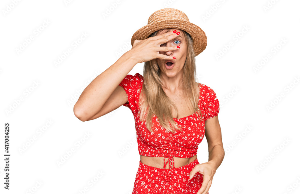 Beautiful caucasian woman wearing summer hat peeking in shock covering face and eyes with hand, looking through fingers with embarrassed expression.