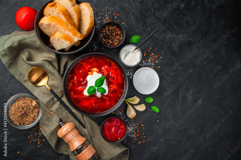 Borscht with sour cream, bread and spices on a black background.