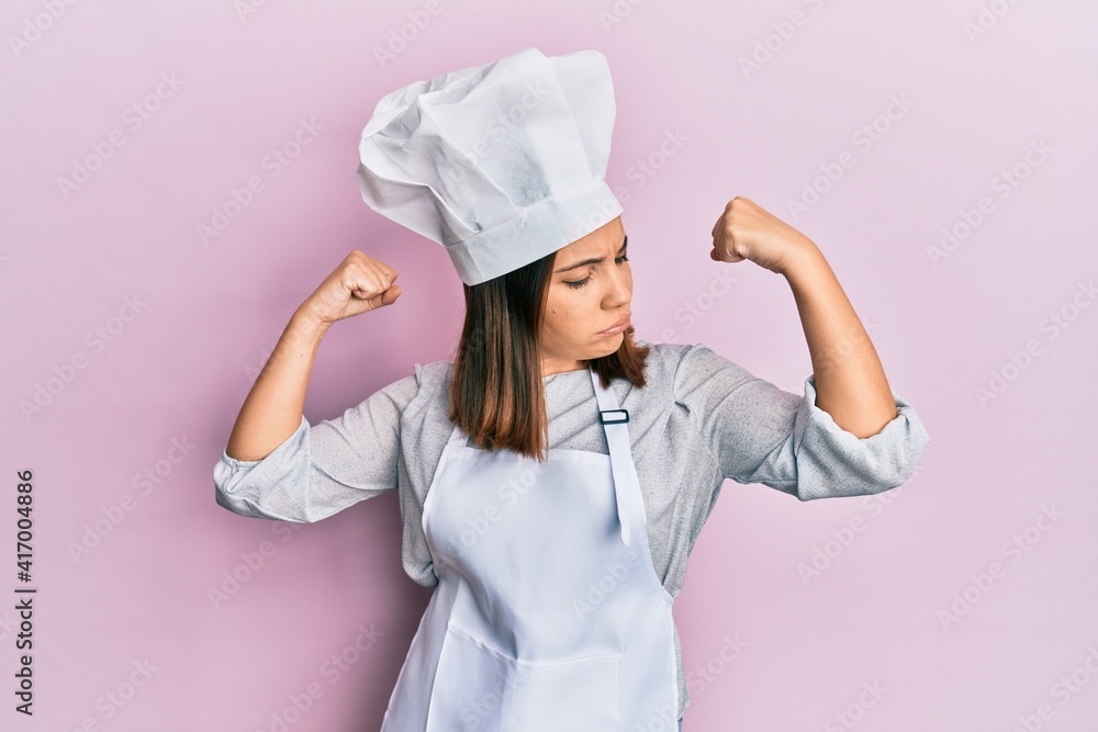 Young beautiful woman wearing professional cook uniform and hat showing arms muscles smiling proud. fitness concept. Young beautiful woman wearing professional cook uniform and hat showing arms muscles smiling proud. fitness concept.