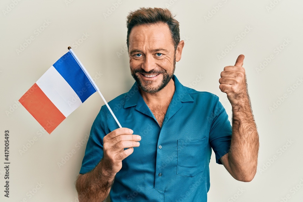 Middle age man holding france flag smiling happy and positive, thumb up doing excellent and approval sign Middle age man holding france flag smiling happy and positive, thumb up doing excellent and approval sign