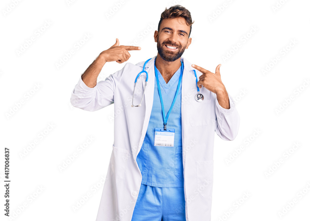 Young hispanic man wearing doctor uniform and stethoscope smiling cheerful showing and pointing with fingers teeth and mouth. dental health concept. Young hispanic man wearing doctor uniform and stethoscope smiling cheerful showing and pointing with fingers teeth and mouth. dental health concept.