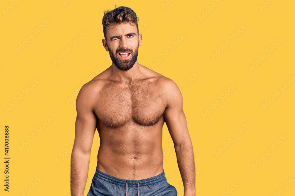 Young hispanic man wearing swimwear shirtless winking looking at the camera with sexy expression, cheerful and happy face.