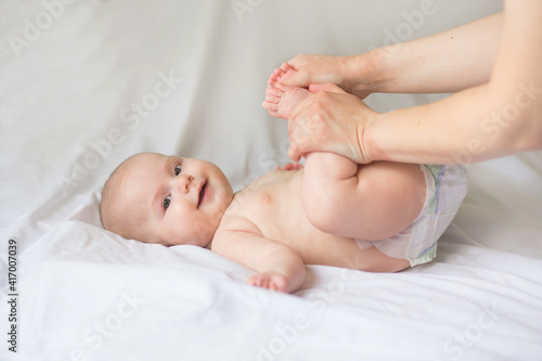 Happy infant girl doing baby massage by his mother at home. Newborn child about 5 months old