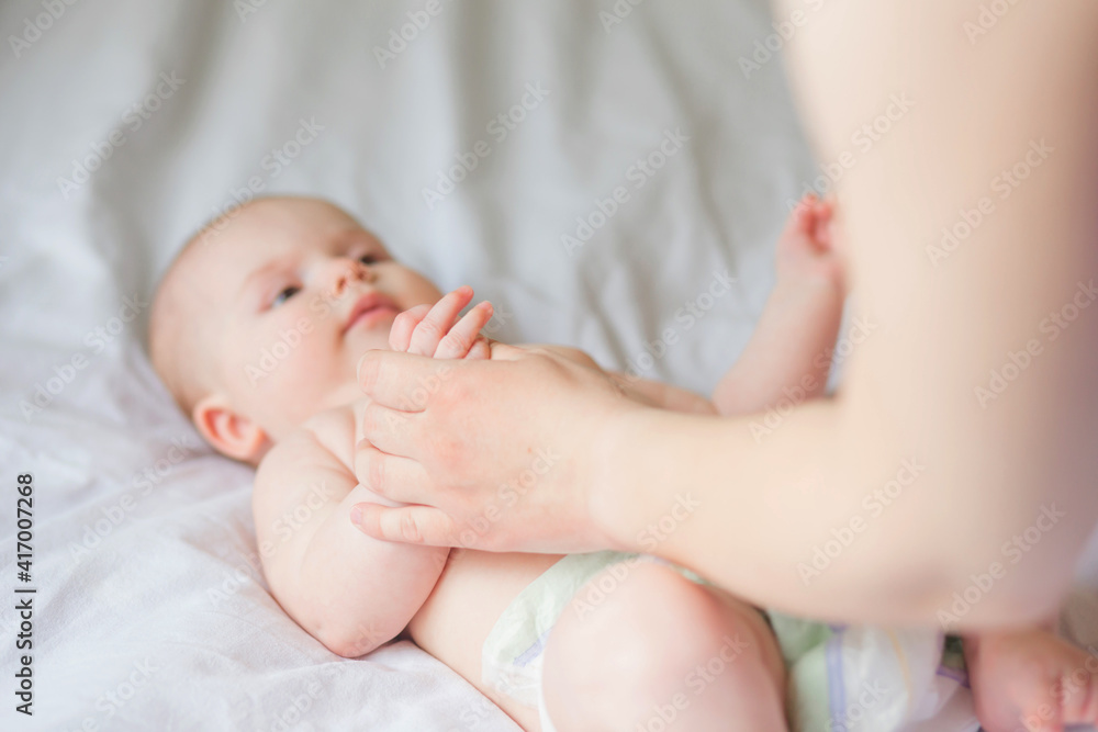 Happy infant girl doing baby massage by his mother at home. Newborn child about 5 months old