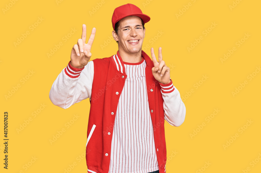 Handsome caucasian man wearing baseball uniform smiling looking to the camera showing fingers doing victory sign. number two. Handsome caucasian man wearing baseball uniform smiling looking to the camera showing fingers doing victory sign. number two.