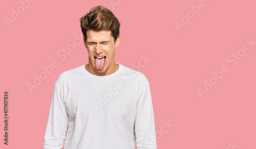 Handsome caucasian man wearing casual white sweater sticking tongue out happy with funny expression. emotion concept.
